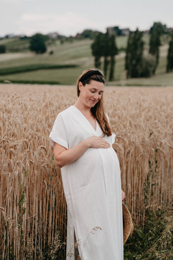 babybauch14 Schwangere Frau steht auf einem Feldweg und hält ihr fließendes Kleid während eines Babybauchshootings in der Natur.