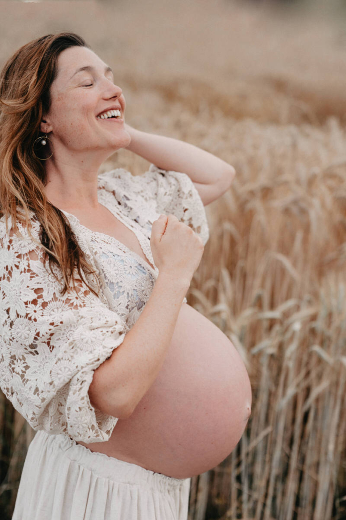 babybauch21 Schwangere Frau steht auf einem Feldweg und hält ihr fließendes Kleid während eines Babybauchshootings in der Natur.
