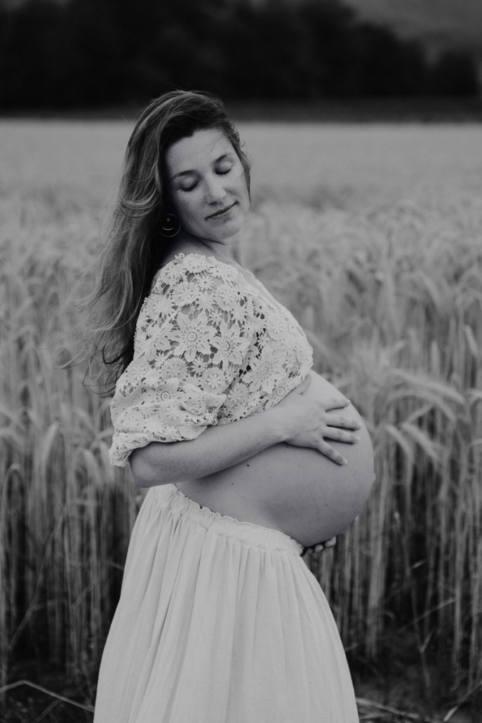 babybauch22 Schwangere Frau steht auf einem Feldweg und hält ihr fließendes Kleid während eines Babybauchshootings in der Natur.