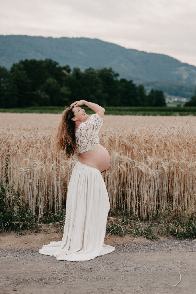 babybauch26 Schwangere Frau steht auf einem Feldweg und hält ihr fließendes Kleid während eines Babybauchshootings in der Natur.