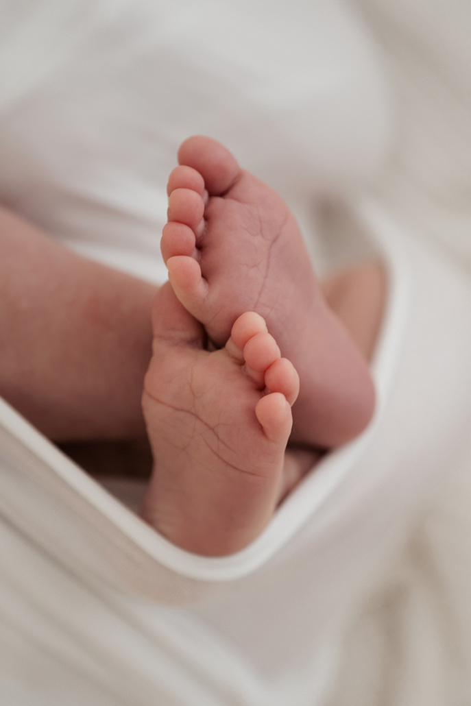 babyfotos3 Detailaufnahme von Babyfüßen, gehalten von der Hand der großen Schwester – zarte Geschwistermomente