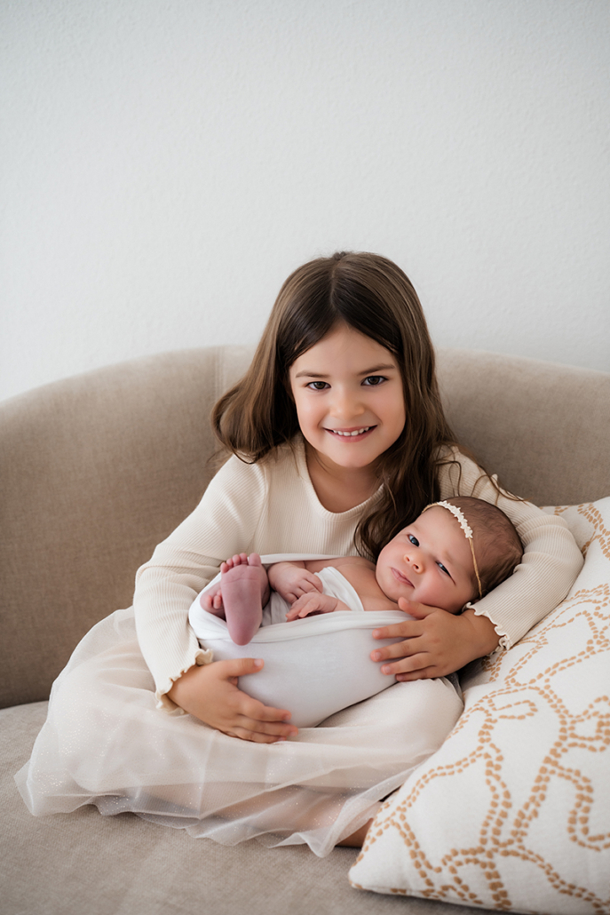 babyfotos4 Fürsorgliche große Schwester hält das Baby im Arm während eines natürlichen Studioshootings.