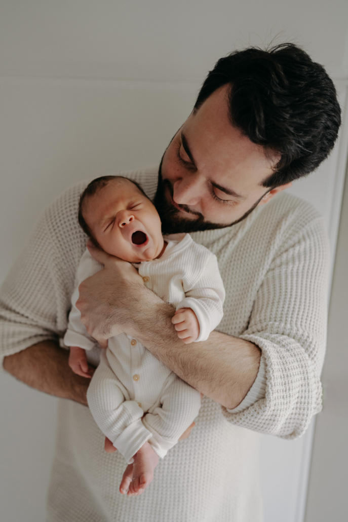 homestory-12 Neugeborenes schläft in den Armen des Vaters bei einer Homestory in der Steiermark. Zeitloses und schlichtes Neugeborenenshooting.