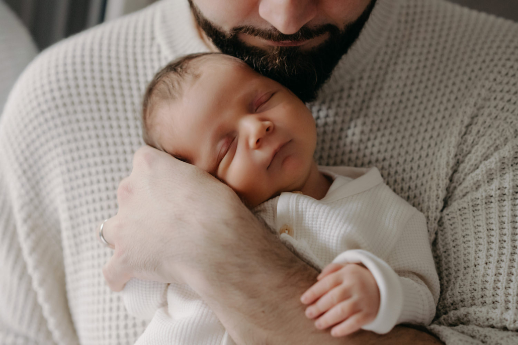 homestory-14 Neugeborenes schläft in den Armen des Vaters bei einer Homestory in der Steiermark. Zeitloses und schlichtes Neugeborenenshooting.