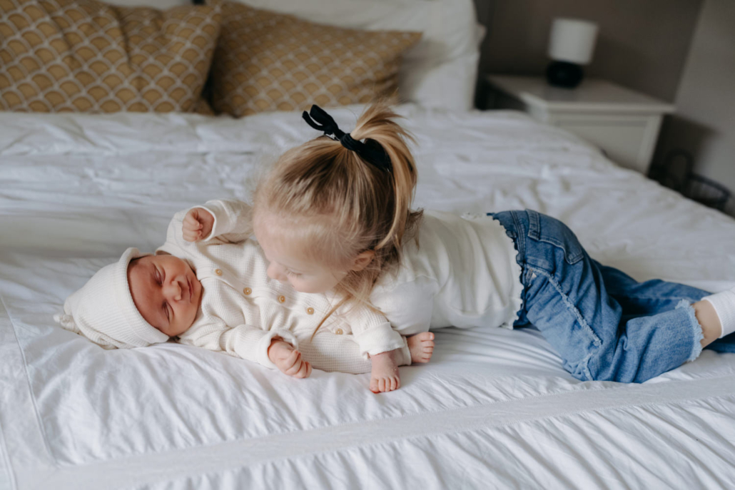 homestory-5 Geschwistermoment: ältere Schwester hält das Neugeborene liebevoll im Arm, authentisches Familienshooting zu Hause.